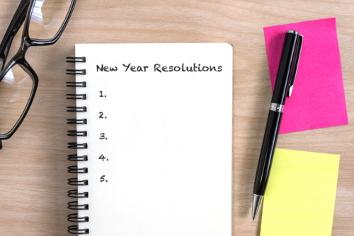 New year resolutions concept with open notebook, pen, colorful sticky note and eye glasses on wooden desk